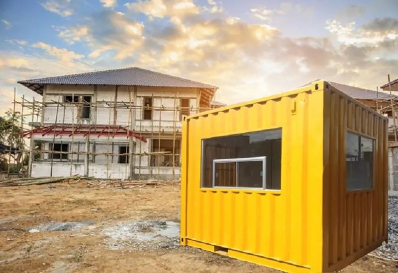 Container văn phòng màu vàng có cửa sổ kính đặt tại khu đất công trình đang xây dựng