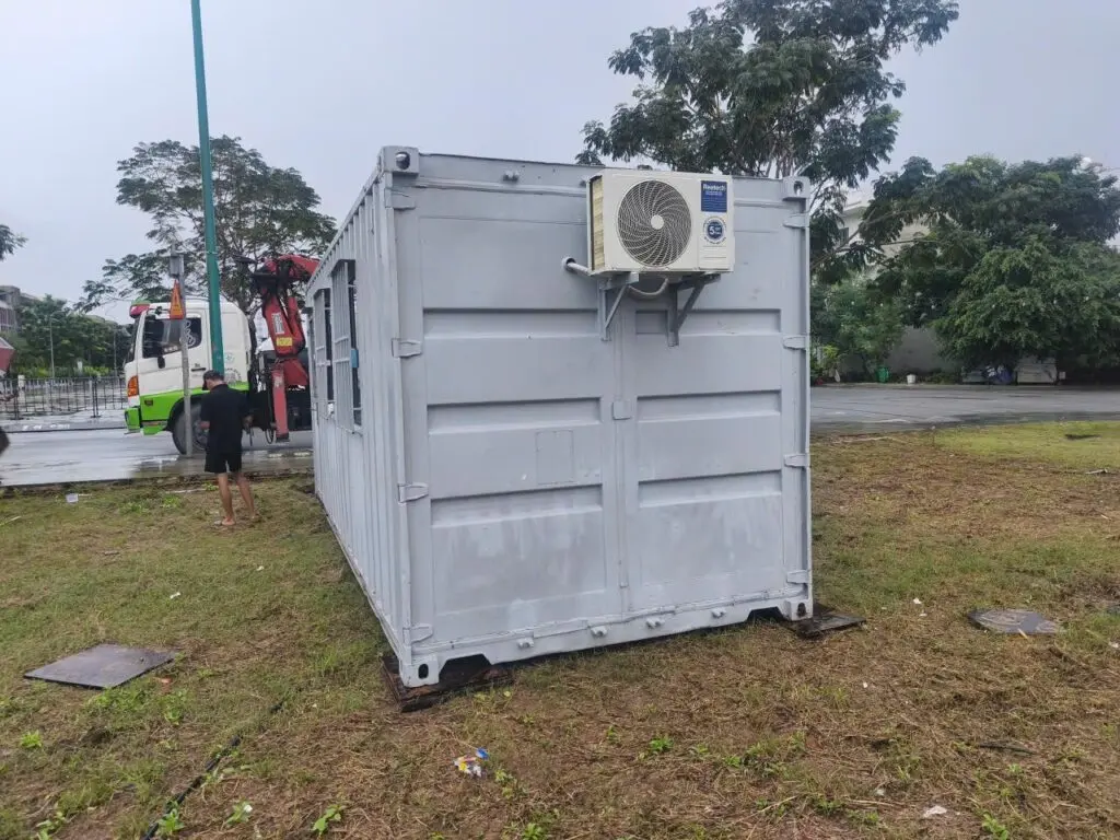 Container văn phòng 20ft sơn xám lắp máy lạnh treo ngoài, xe cẩu đứng phía sau tại Global City