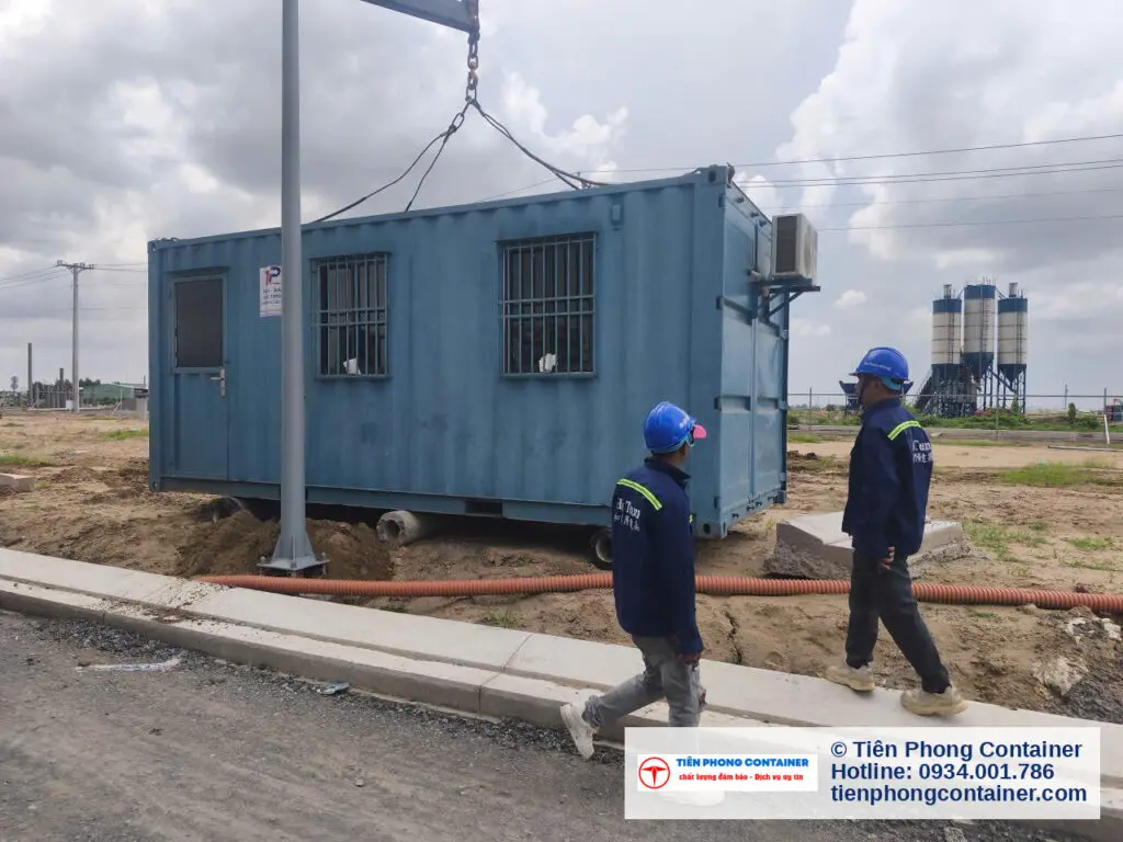 Container văn phòng 20ft xanh ngọc đặt cạnh đường nội bộ, hai công nhân đi ngang kiểm tra