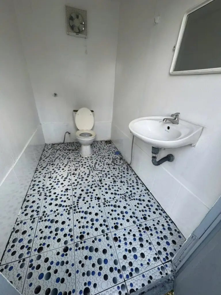 Góc buồng vệ sinh có bồn cầu, lavabo và quạt thông gió trong container 20ft tại Lâm Đồng