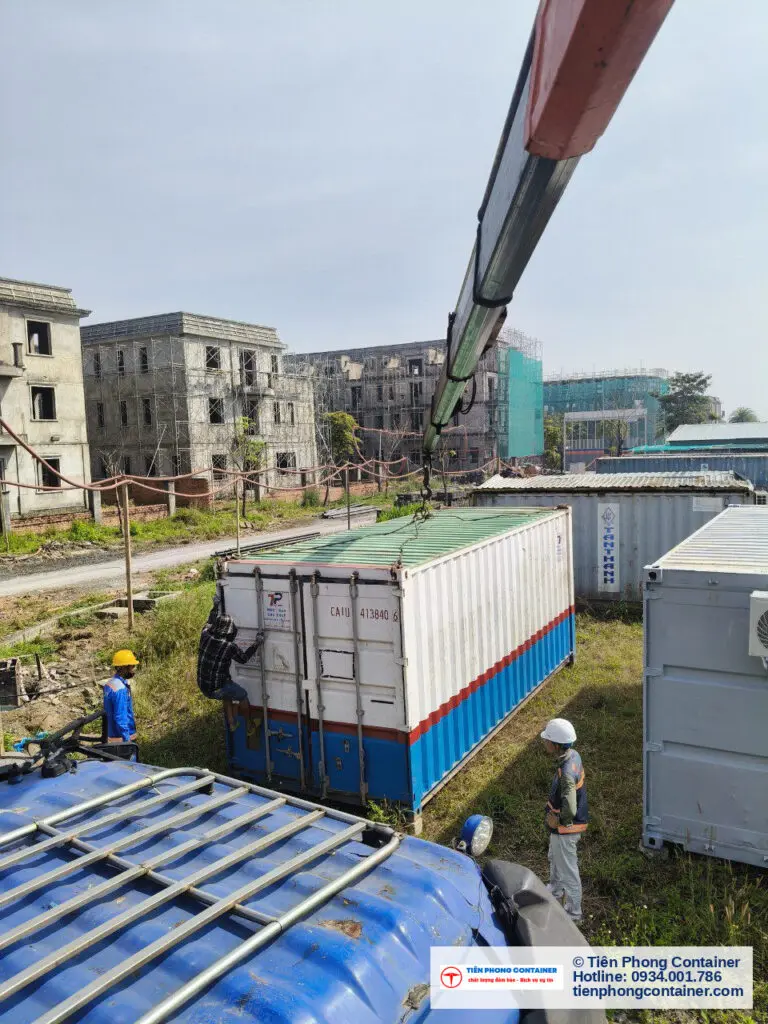 Kỹ thuật viên điều khiển cần cẩu hạ container tại Aqua City, nền là dãy nhà phố đang xây dựng