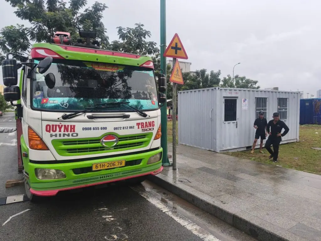 Xe tải gắn cẩu đứng trên đường Global City trong ngày mưa, container văn phòng 20ft phía sau