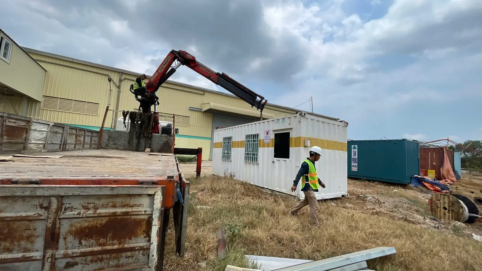 Xe tải gắn cẩu hạ container văn phòng sơn trắng vạch vàng cạnh nhà xưởng KCN Phú Mỹ 1