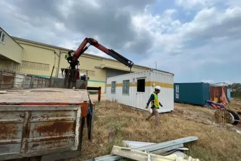 Xe tải gắn cẩu hạ container văn phòng sơn trắng vạch vàng cạnh nhà xưởng KCN Phú Mỹ 1